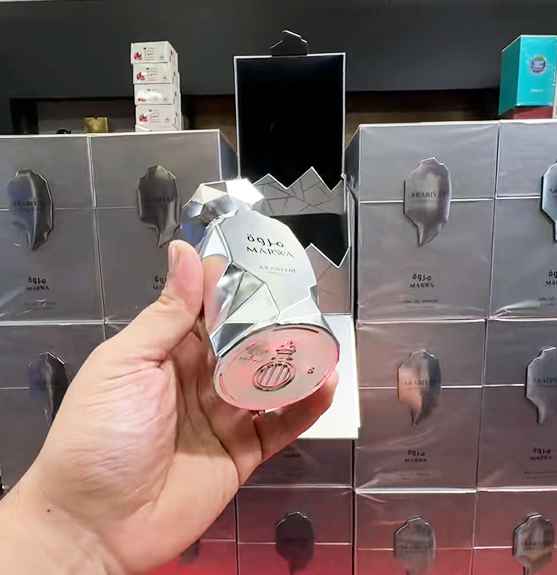 Arabiyat Prestige Marwa perfume sobre una mesa de madera siendo observado por un hombre con traje elegante